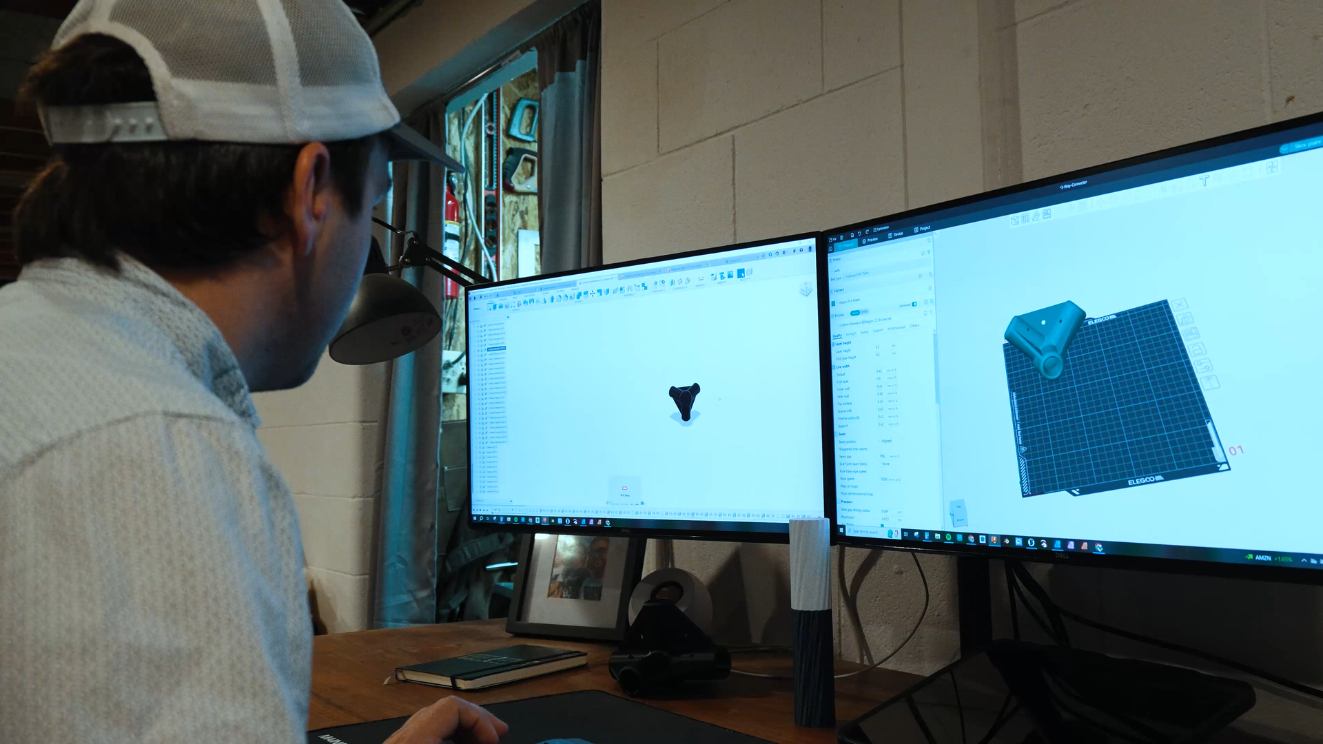 Person working at a desk with two computer monitors displaying 3D models.